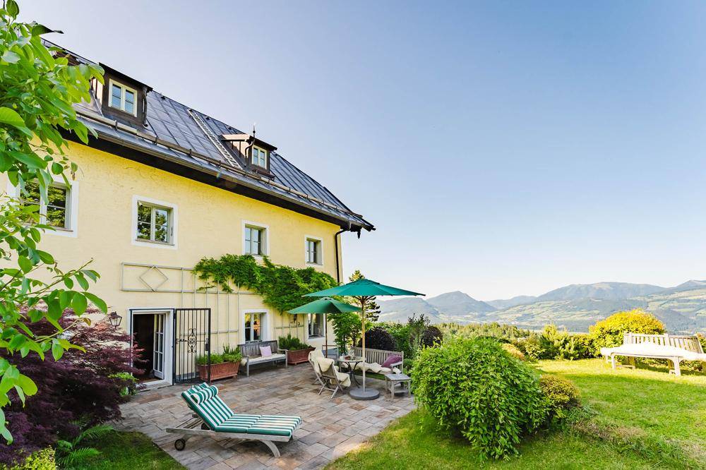 Geräumige Terrasse mit Gartenmöbeln und Sonnenschirmen, umgeben von Grün und mit Bergblick.