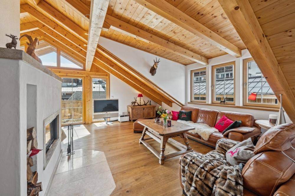 Gemütliches Wohnzimmer mit Ledersofa, Kamin und großen Fenstern, die viel Licht hereinlassen.