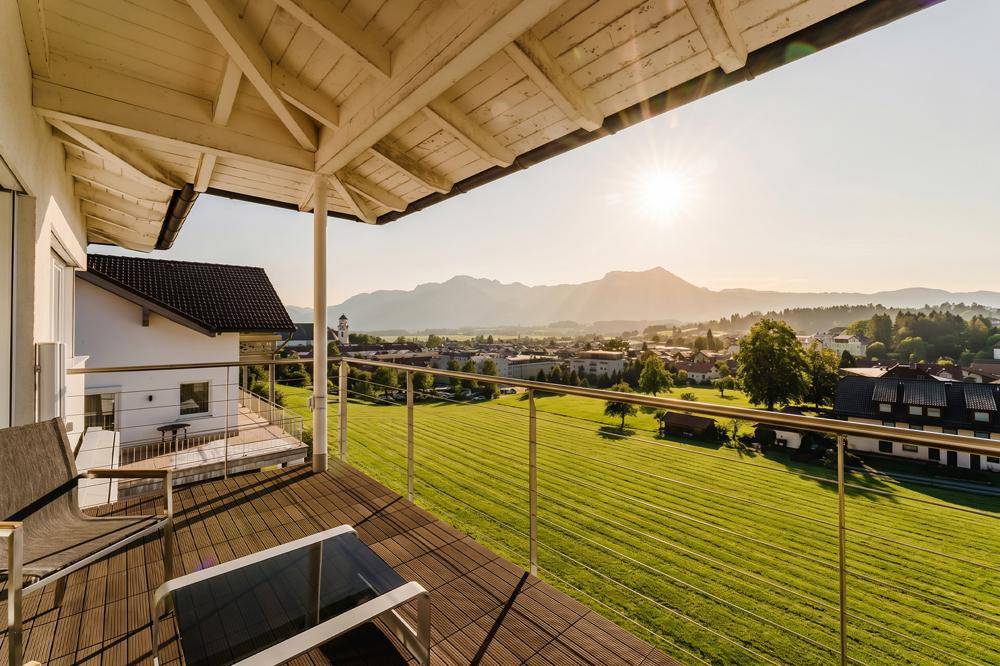 Überdachter Balkon mit Holzboden, Sitzgelegenheiten und Panoramablick auf Berge und Stadt.