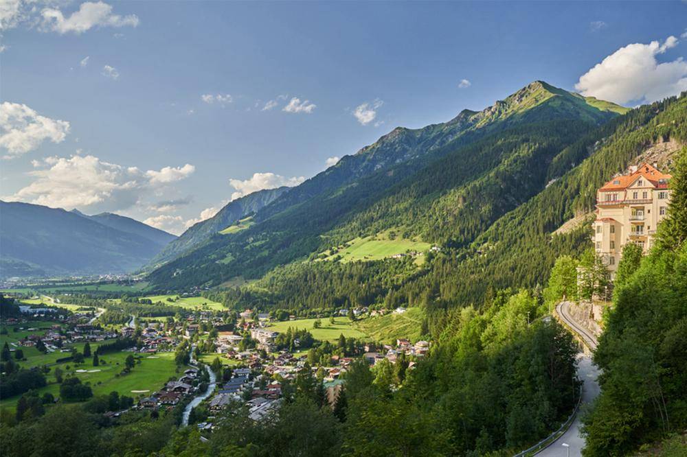 Panoramablick auf ein malerisches Tal mit einem Dorf und einem historischen Gebäude am Berghang.