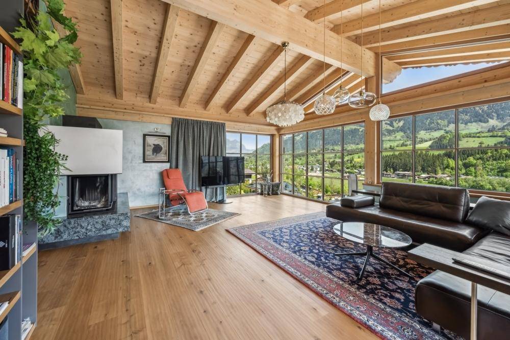Geräumiges Wohnzimmer mit Kamin, Holzboden und atemberaubendem Blick auf die Alpenlandschaft.
