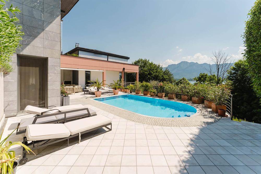 Sonnige Poolterrasse mit Liegestühlen, umgeben von Pflanzen und mit Blick auf die Berglandschaft.