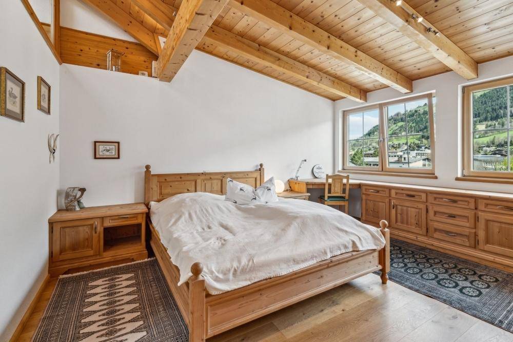 Helles Schlafzimmer mit Holzbett, passenden Möbeln und weitem Blick auf die umliegende Landschaft.