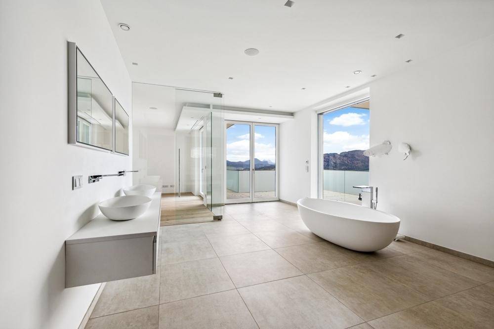Modernes Badezimmer mit freistehender Badewanne, Doppelwaschbecken und Bergblick durch große Fenster.