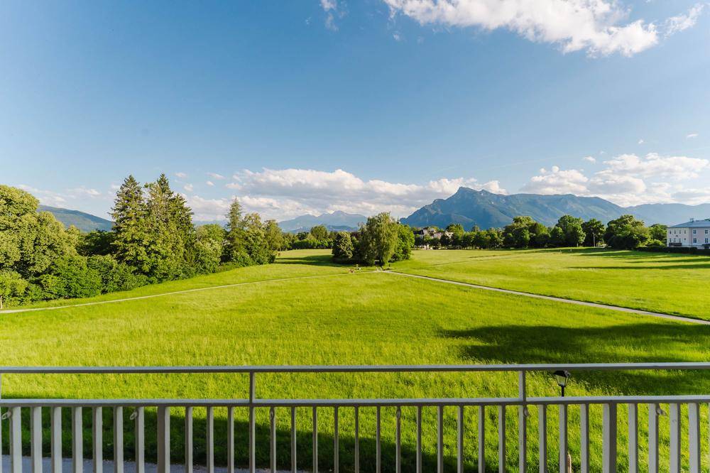 Weitläufiger Blick vom Balkon über grüne Wiesen und majestätische Berge.