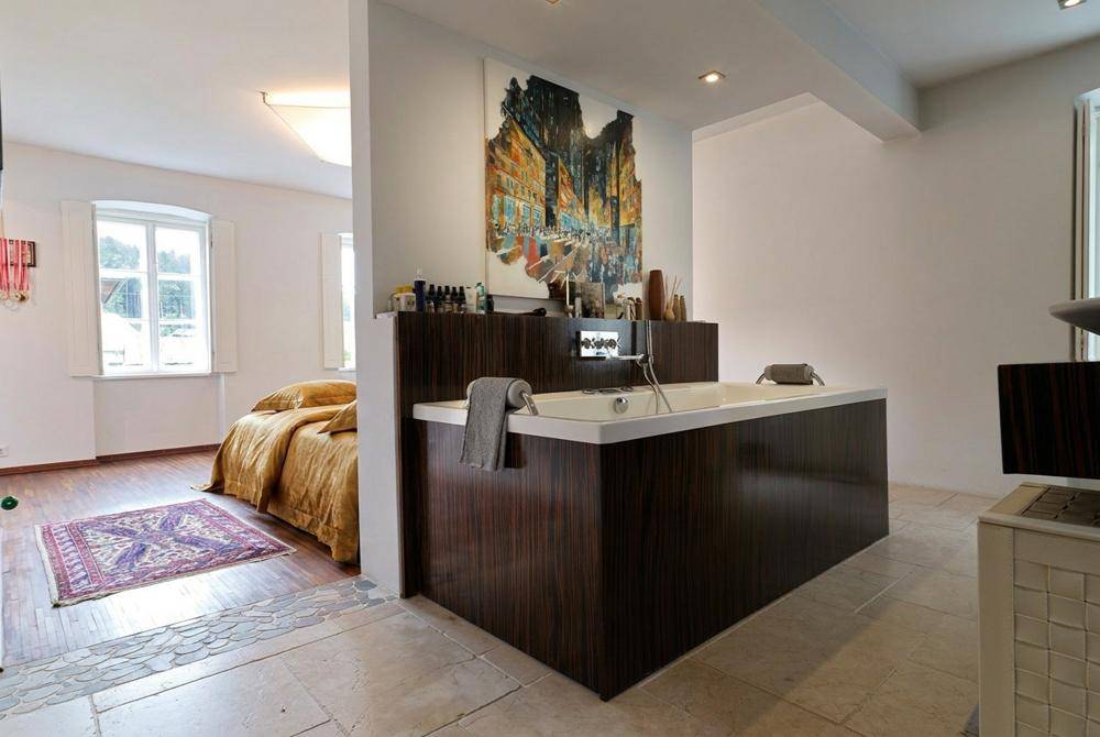 Geräumiges Schlafzimmer mit integrierter Badewanne und Holzboden, getrennt durch eine Trennwand.