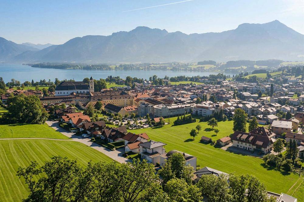 Malerische Stadtansicht mit See, Bergen und historischen Gebäuden unter blauem Himmel.