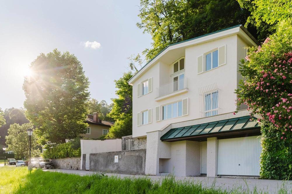 Sonniges Wohnhaus mit weißer Fassade, grünen Fensterläden und integrierter Garage.