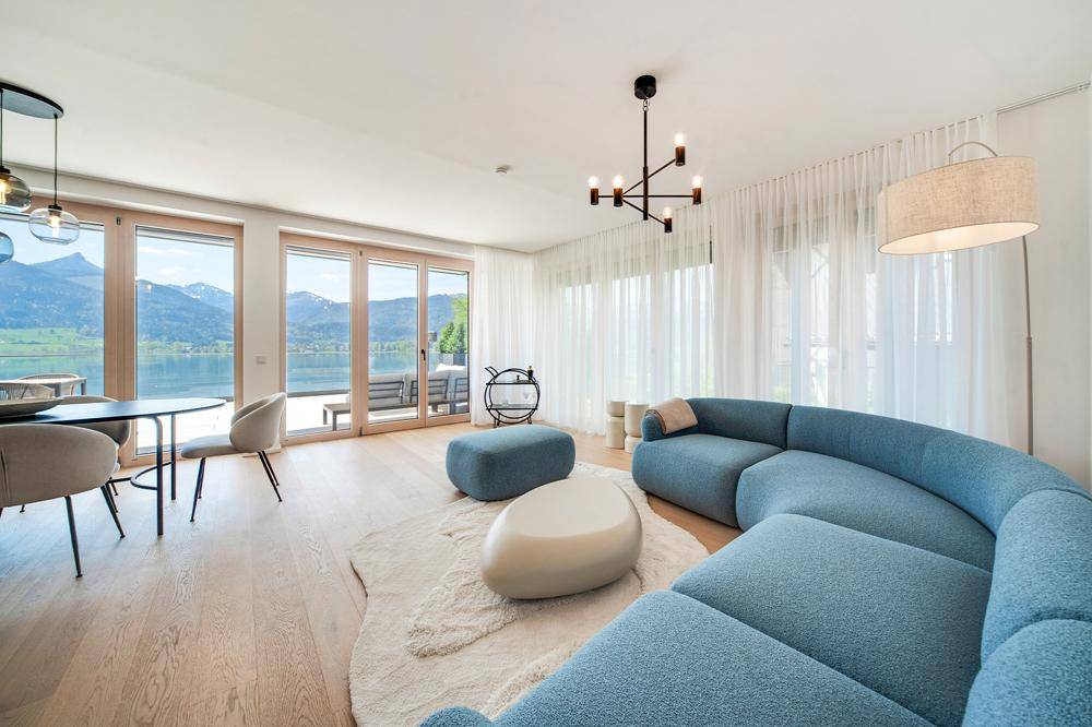 Helles, offenes Wohn-Esszimmer mit modernem Sofa, Holzboden und großen Fenstern mit Seeblick.