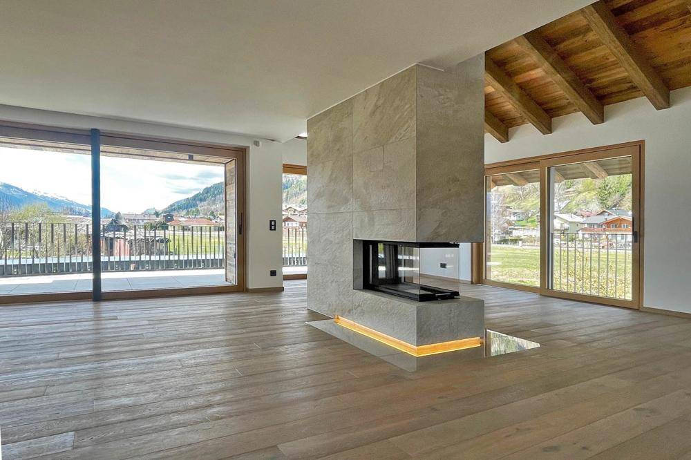 Geräumiger Wohnbereich mit Holzboden, freiliegenden Holzbalken, modernem Kamin und Bergblick.