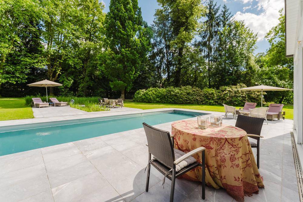 Gemütlicher Sitzbereich auf der Terrasse neben dem Pool mit Esstisch und Sonnenliegen im Hintergrund.
