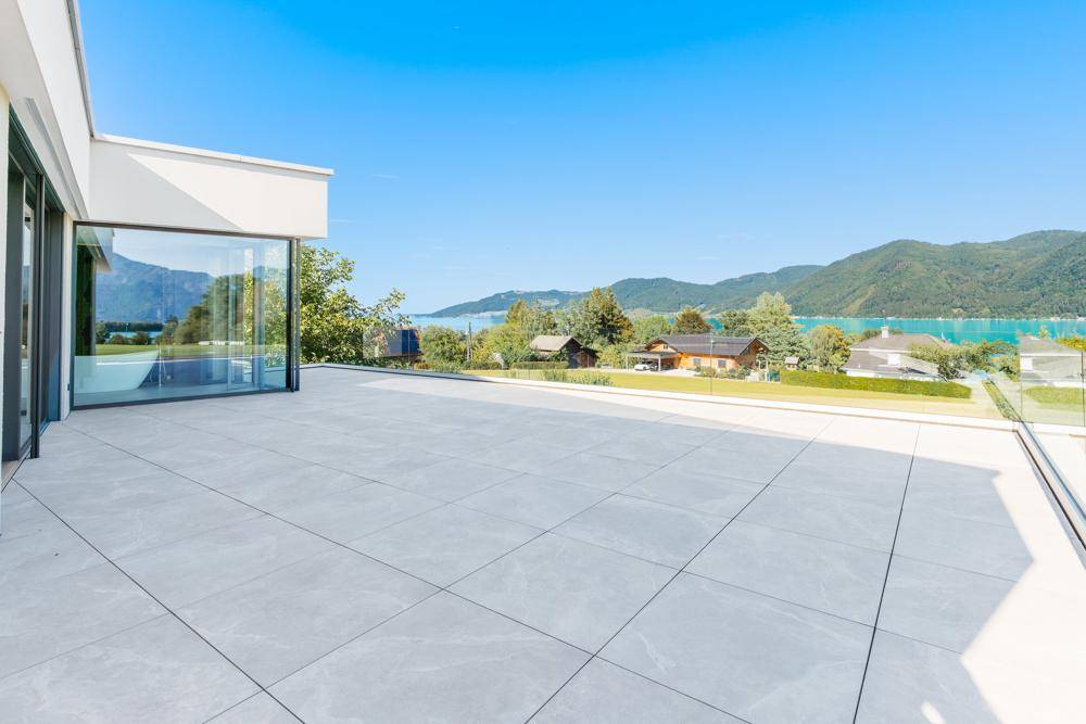 Weitläufige Dachterrasse mit Fliesenboden und atemberaubendem Blick auf den See und die umliegenden Berge.