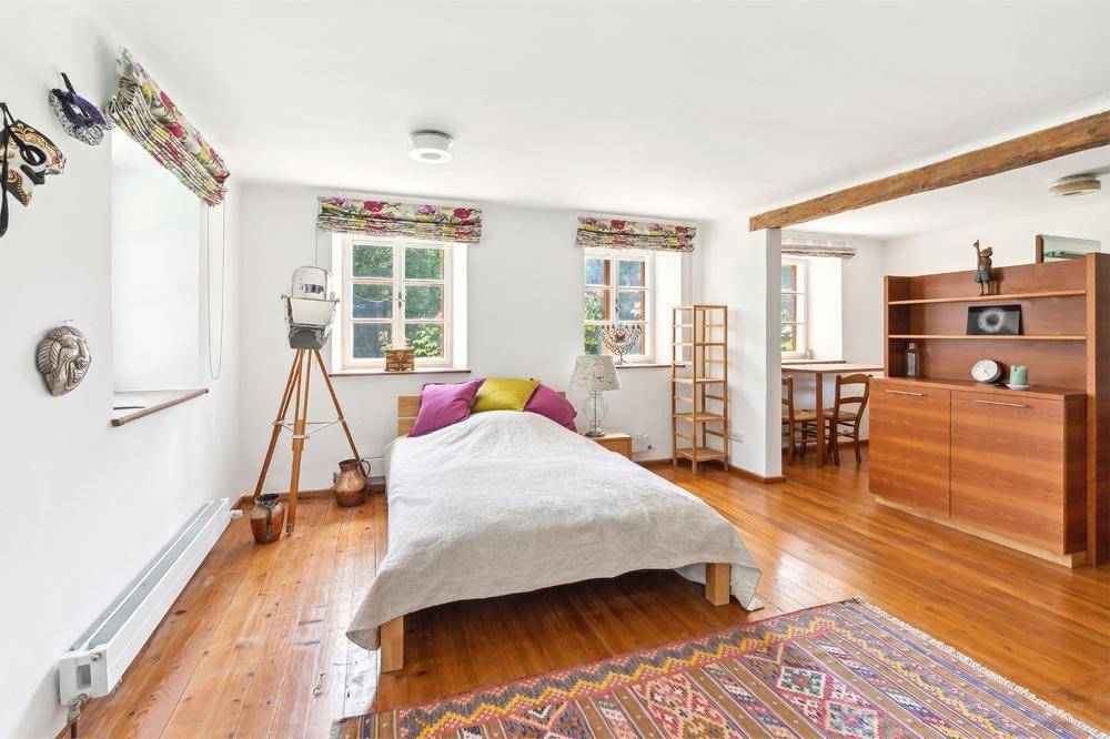 Helles Schlafzimmer mit Holzboden, zwei Fenstern und einem angrenzenden Essbereich.