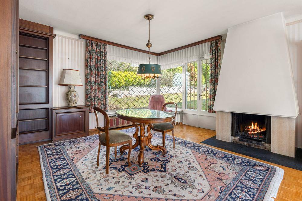 Gemütlicher Essbereich mit Kamin, Erkerfenster und traditionellen Möbeln, umgeben von einem Teppich.