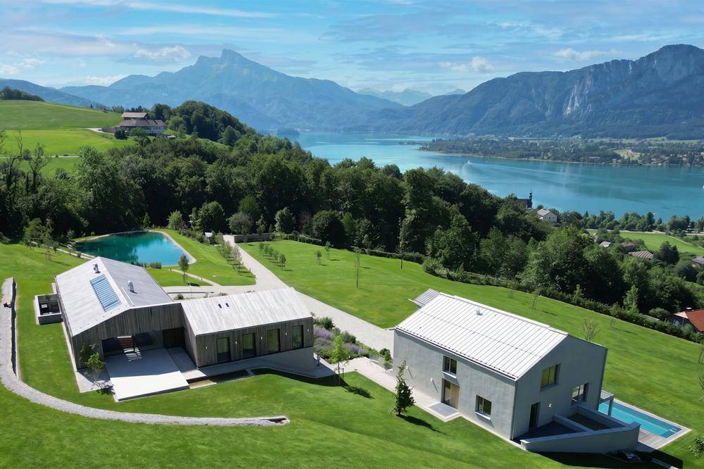 Weitläufige Immobilienanlage mit modernen Gebäuden, einem Pool und beeindruckendem Panorama auf See und Berge.