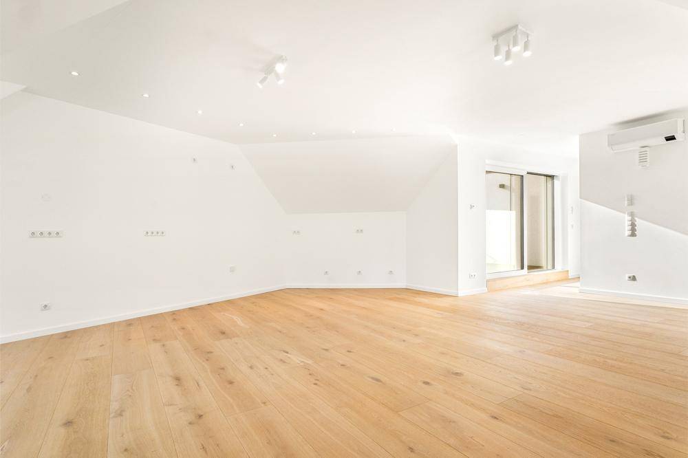 Heller Dachgeschossraum mit Holzboden, Klimaanlage und Zugang zu einem weiteren Bereich.