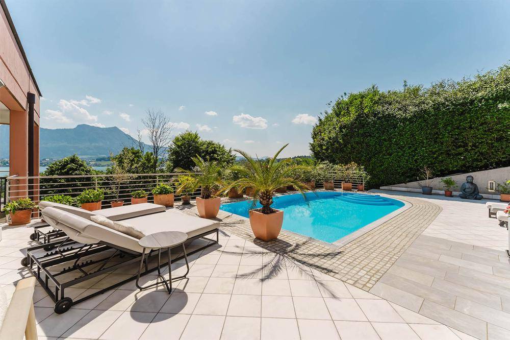 Sonnige Poolterrasse mit Liegestühlen, umgeben von Pflanzen und mit Blick auf die Berglandschaft.