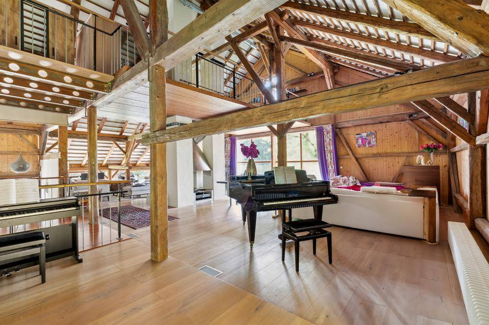 Geräumiges Wohnzimmer mit hohen Decken, freiliegenden Holzbalken und einem Flügel.