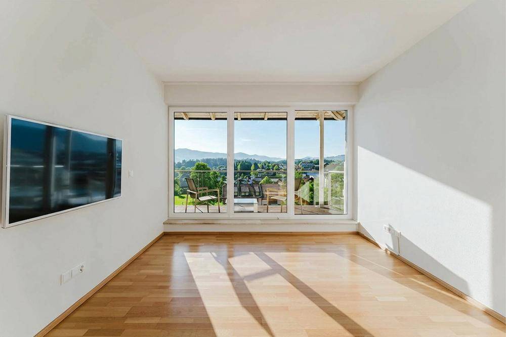 Helles Schlafzimmer mit Holzboden, großer Fensterfront und weitem Blick ins Grüne.