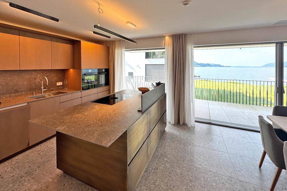 Moderne Küche mit Kochinsel, integrierten Geräten und direktem Zugang zur Terrasse mit Seeblick.