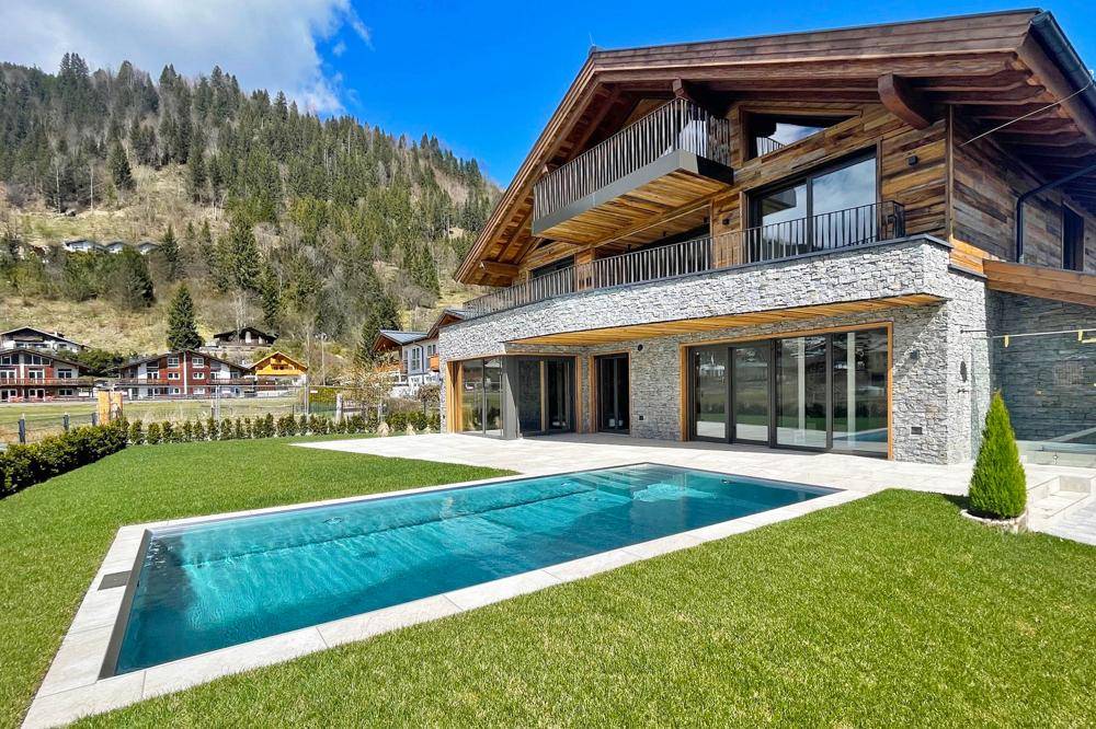 Luxuriöses Chalet mit Außenpool, gepflegtem Rasen und beeindruckendem Bergblick im Frühling.