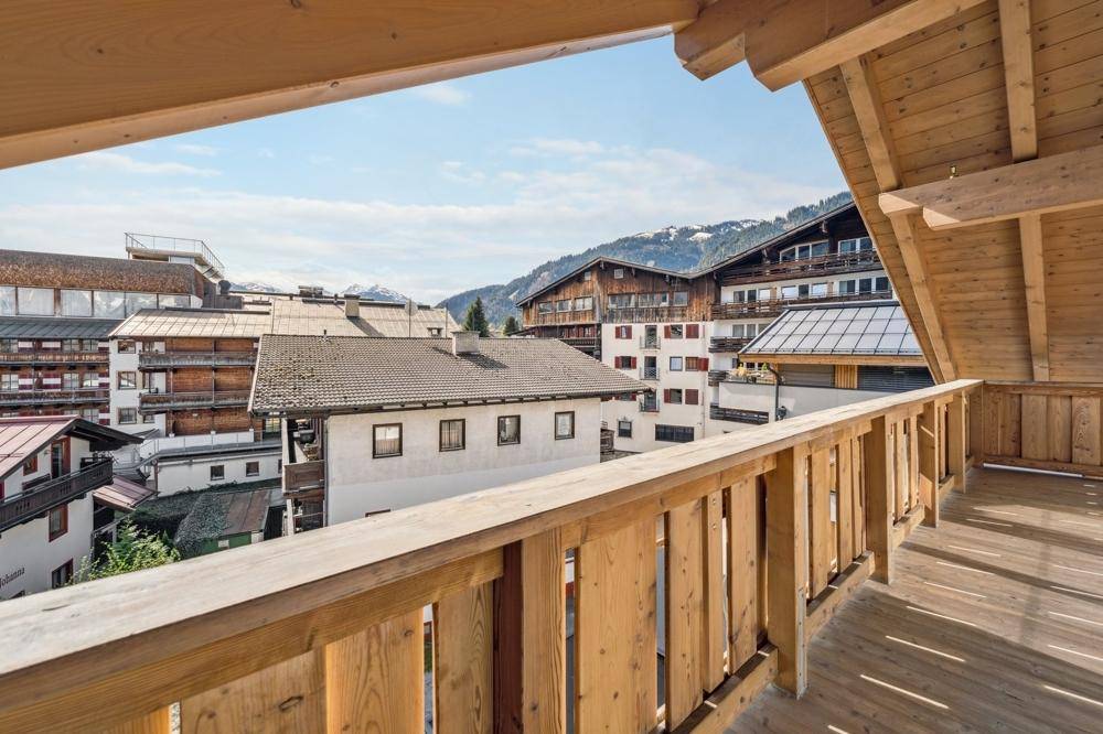 Geräumiger Holzbalkon mit weitem Blick über die Dächer der Nachbargebäude und die Berge.