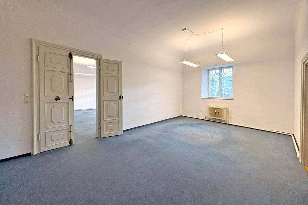Helles Zimmer mit blauem Teppichboden, hohen Flügeltüren und einem Fenster.