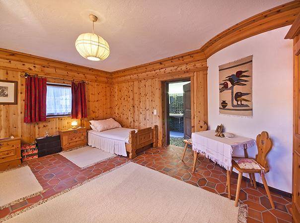 Helles Schlafzimmer mit Holzvertäfelung, Einzelbett und Zugang zu einem weiteren Raum.