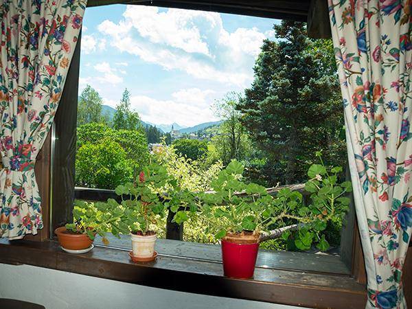Blick aus einem Fenster mit floralen Vorhängen auf eine grüne Landschaft und Berge.
