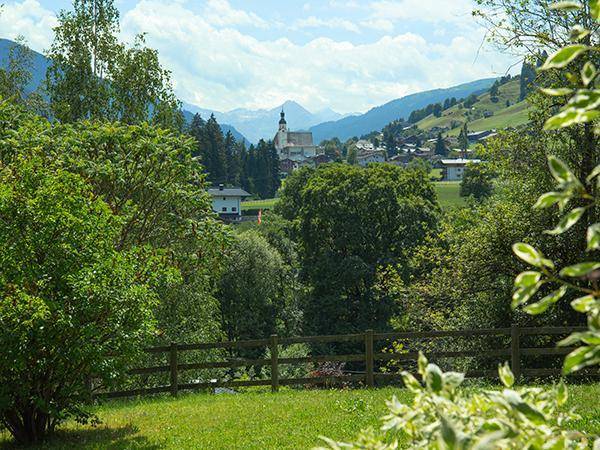 Malerischer Blick auf ein Dorf mit Kirche und die umliegende grüne Berglandschaft.