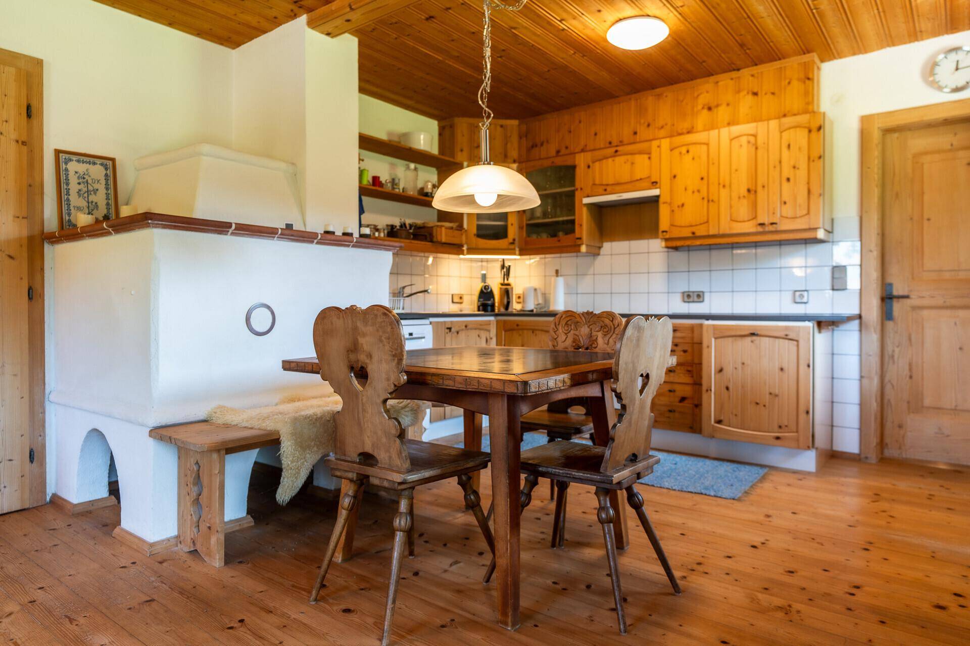 Traditionelle Holzküche mit Essbereich, Kachelofen und rustikalen Holzmöbeln unter einer Holzdecke.