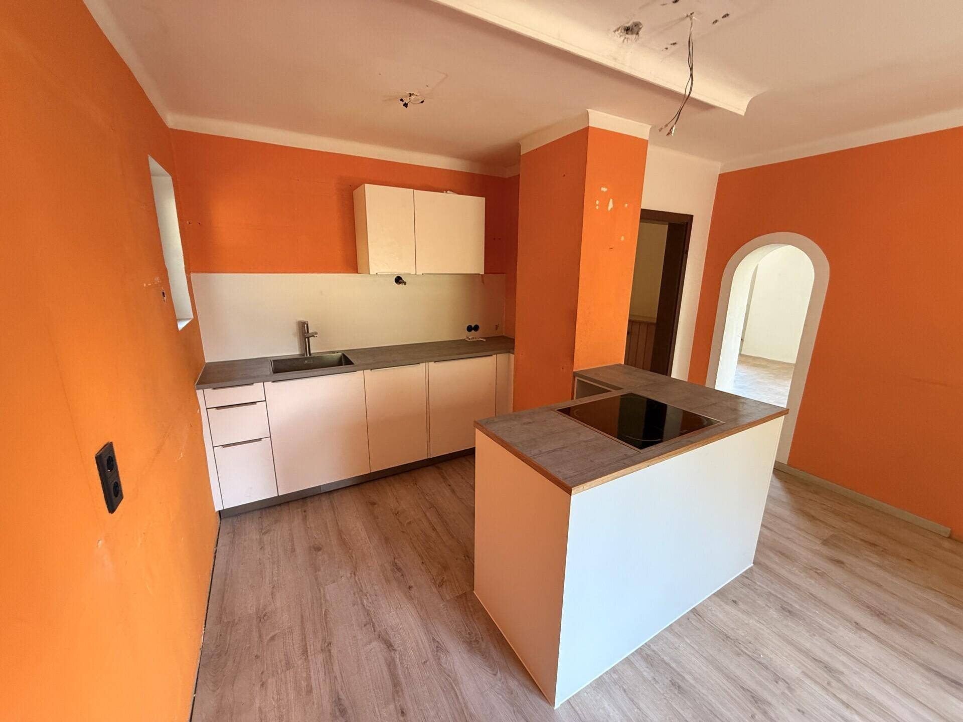 Unfertige Küche mit orangefarbenen Wänden, einer Kücheninsel und einem Induktionskochfeld.