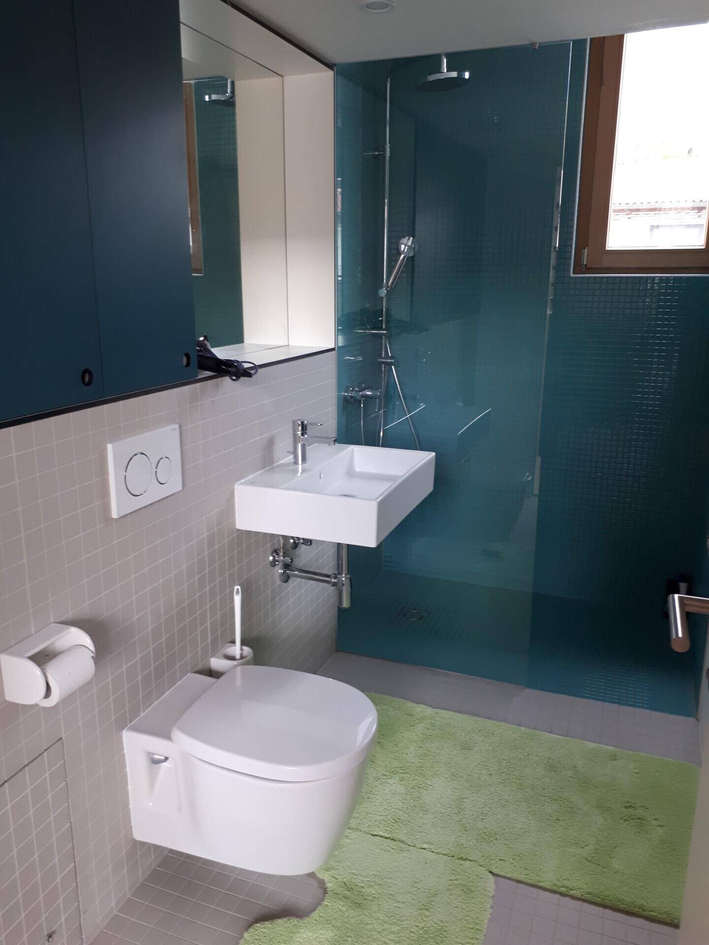 Modernes Badezimmer mit Duschbereich, wandhängendem WC und Fenster für Tageslicht.