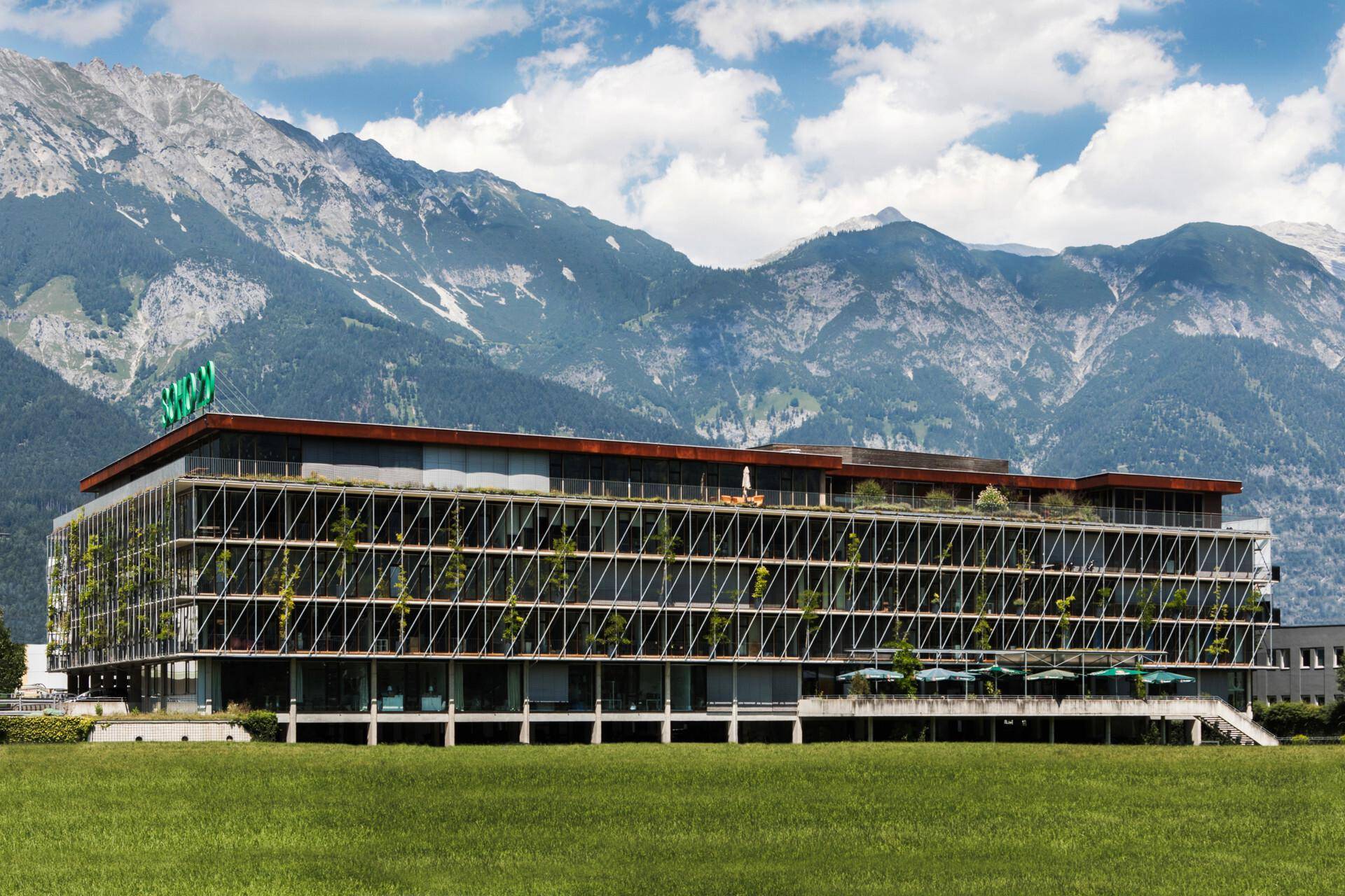Modernes Bürogebäude mit begrünten Fassaden und Alpenpanorama im Hintergrund.