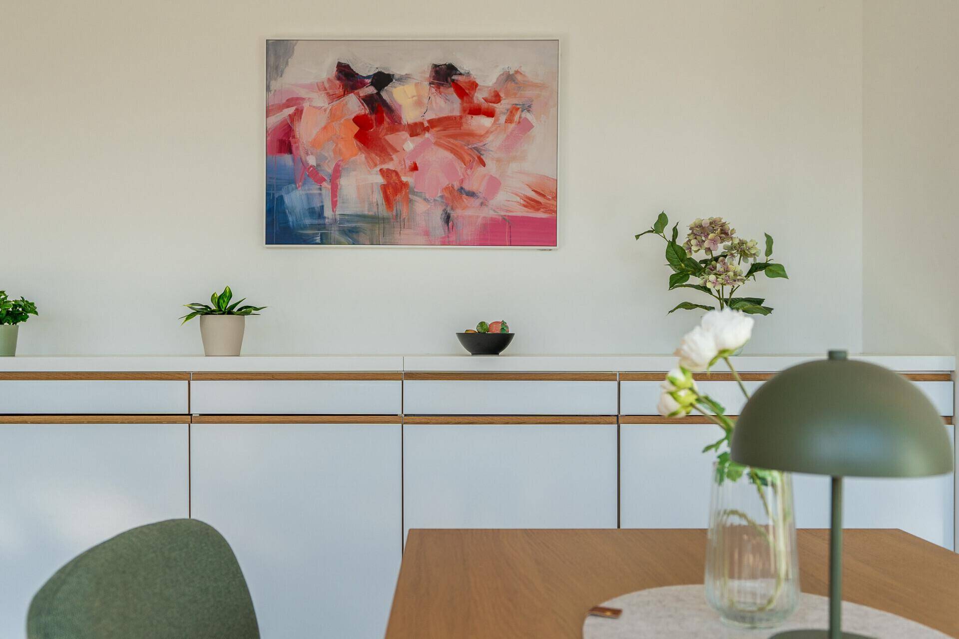 Detailansicht der modernen Küche mit weißen Schränken und farbenfrohem Kunstwerk an der Wand.