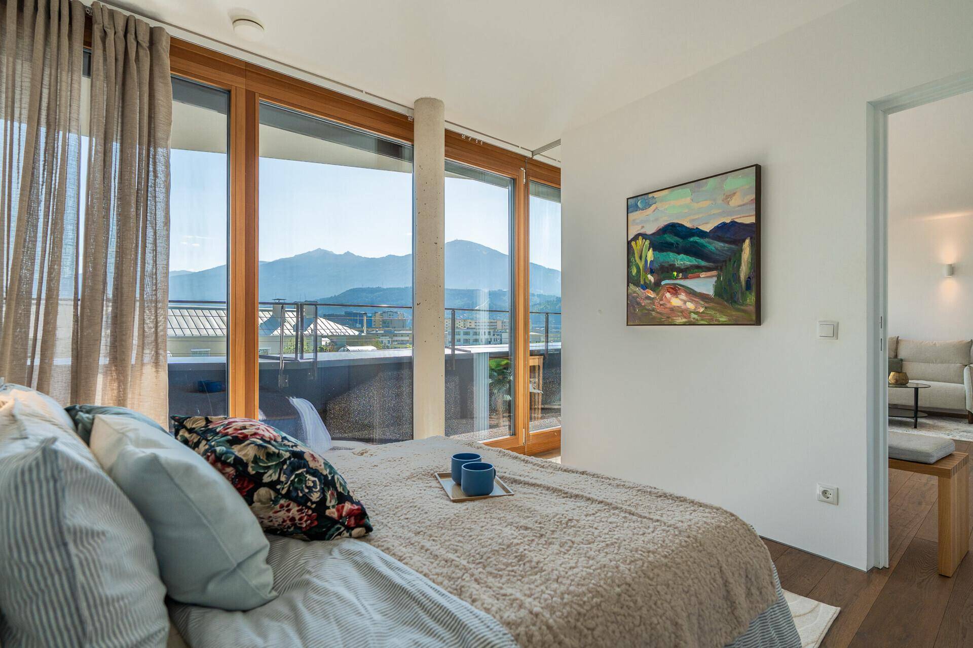 Schlafzimmer mit großem Bett, Holzboden und bodentiefen Fenstern mit Bergblick.