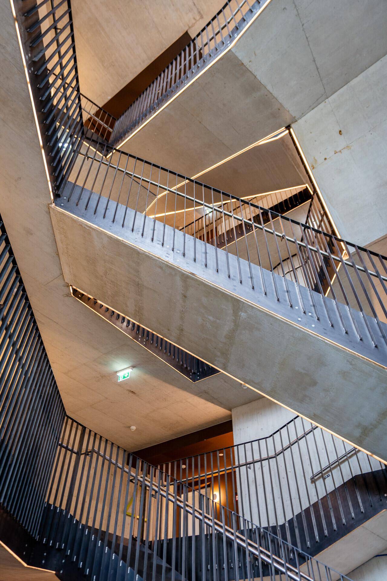 Modernes Treppenhaus mit Betonstufen, Metallgeländer und indirekter Beleuchtung, das mehrere Etagen verbindet.