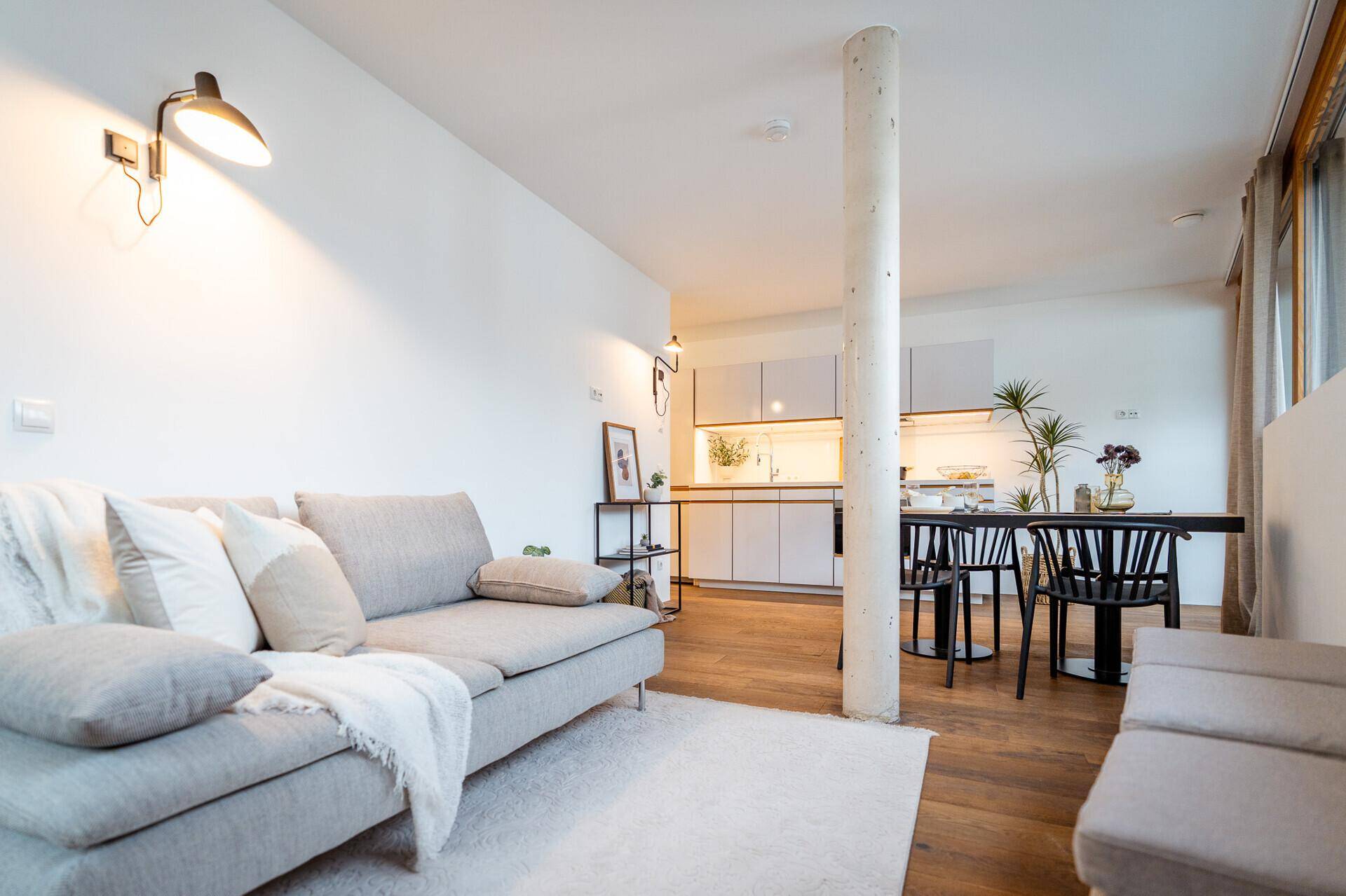 Gemütlicher Wohnbereich mit Sofa, Holzboden und Blick auf den Essbereich sowie die offene Küche.