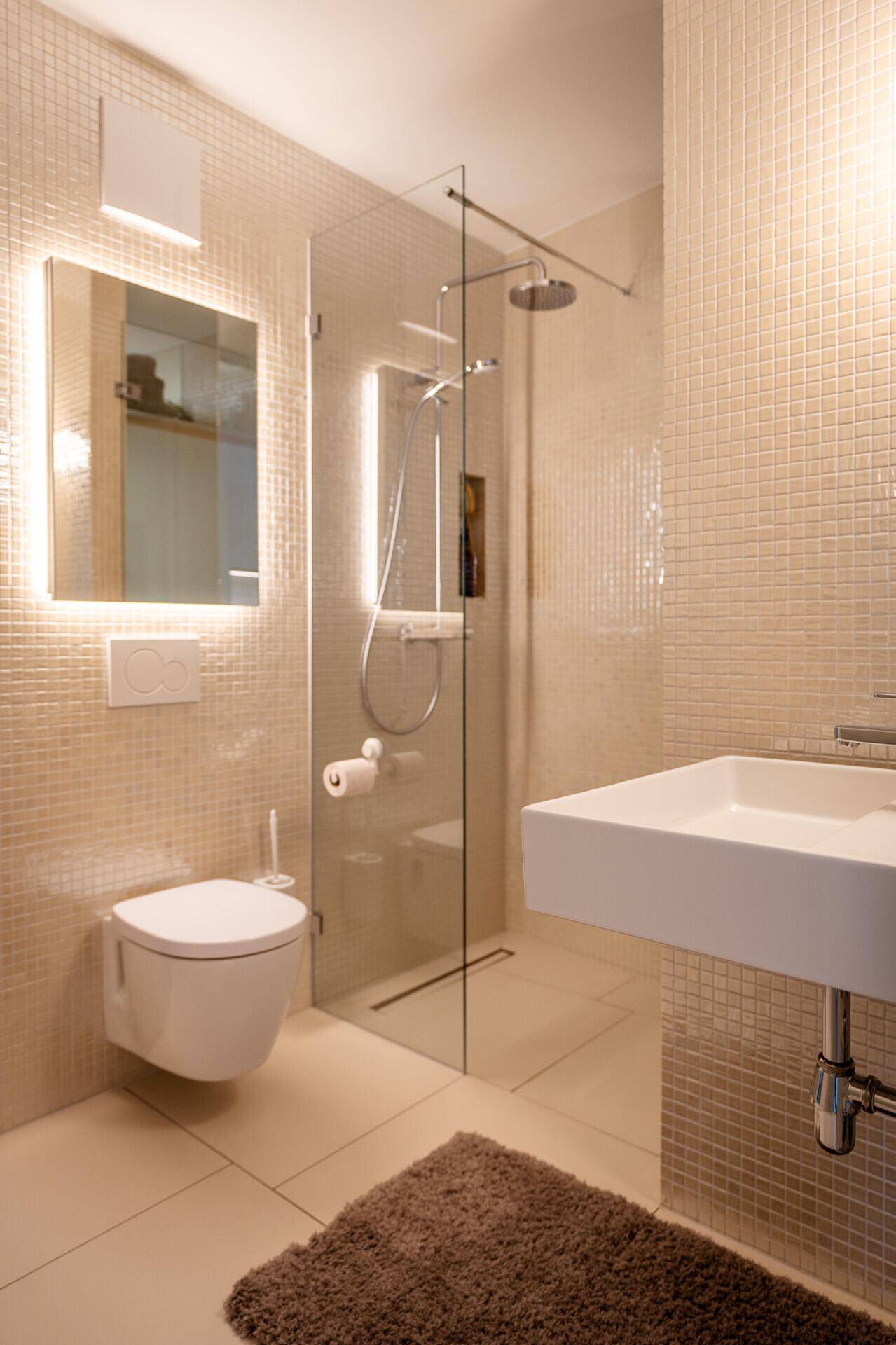 Modernes Badezimmer mit begehbarer Dusche, Wand-WC und stilvollen Mosaikfliesen in hellem Beige.