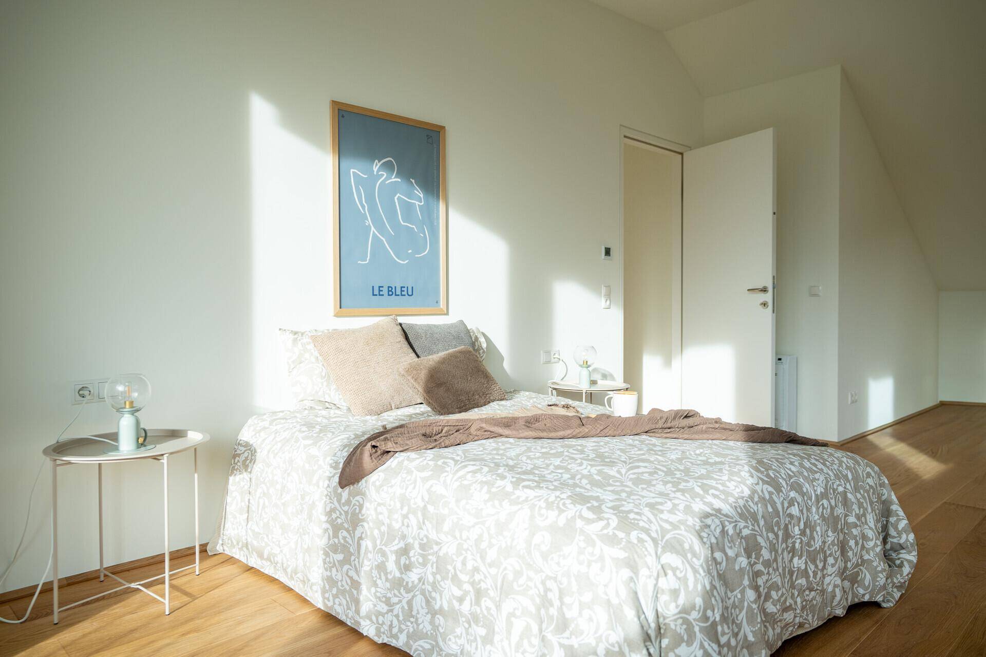 Helles Schlafzimmer mit Holzboden, einem Doppelbett und einer Dachschräge, durchflutet von Sonnenlicht.
