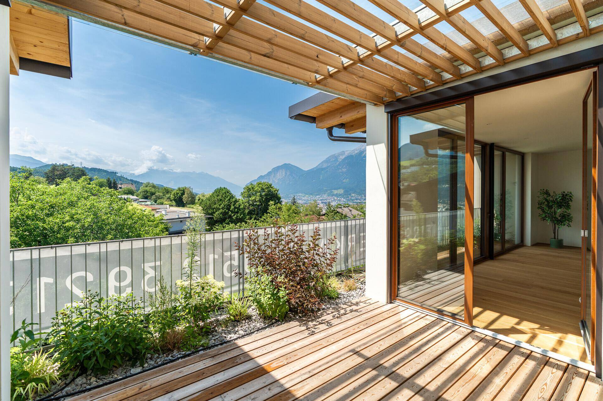 Geräumige Holzterrasse mit Pergola und Schiebetüren, die einen nahtlosen Übergang zum Innenbereich schaffen.