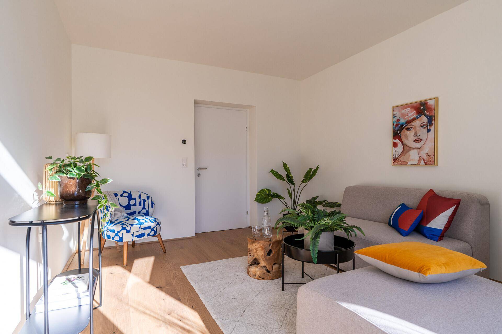 Gemütliches Wohnzimmer mit hellem Holzboden, Kunstwerk und farbigen Kissen.
