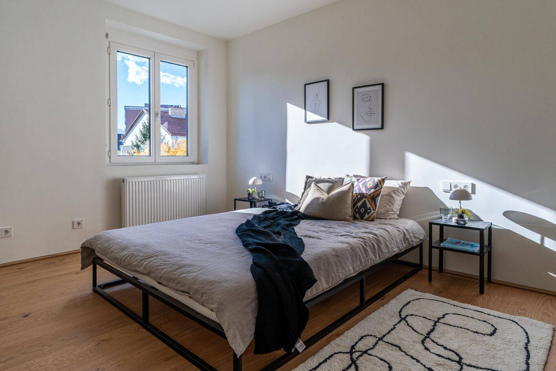 Helles Schlafzimmer mit Holzboden, großem Fenster und minimalistischer Einrichtung.