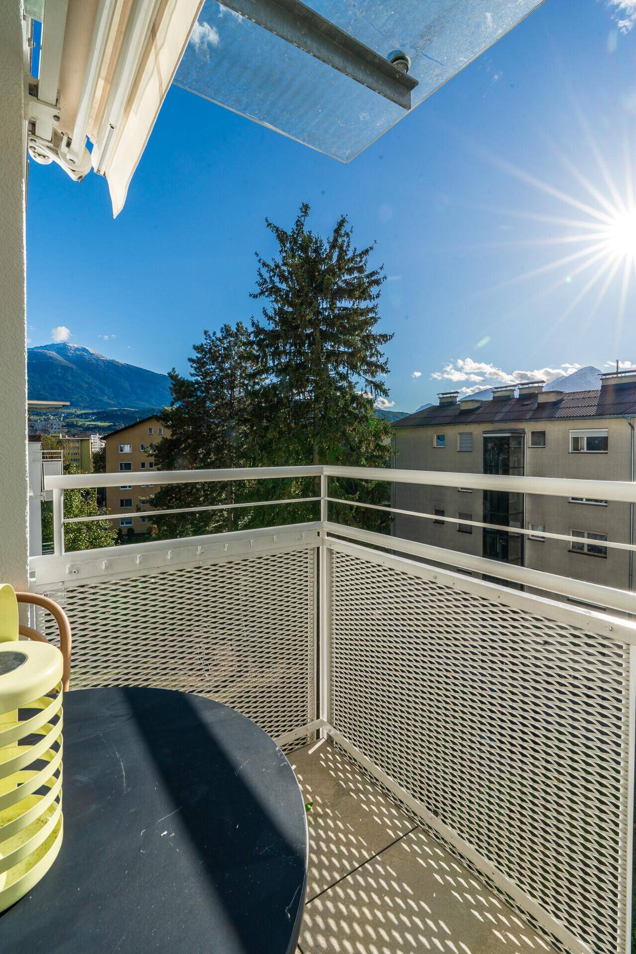 Sonniger Balkon mit Metallgeländer und Blick auf die Berge und umliegende Gebäude.