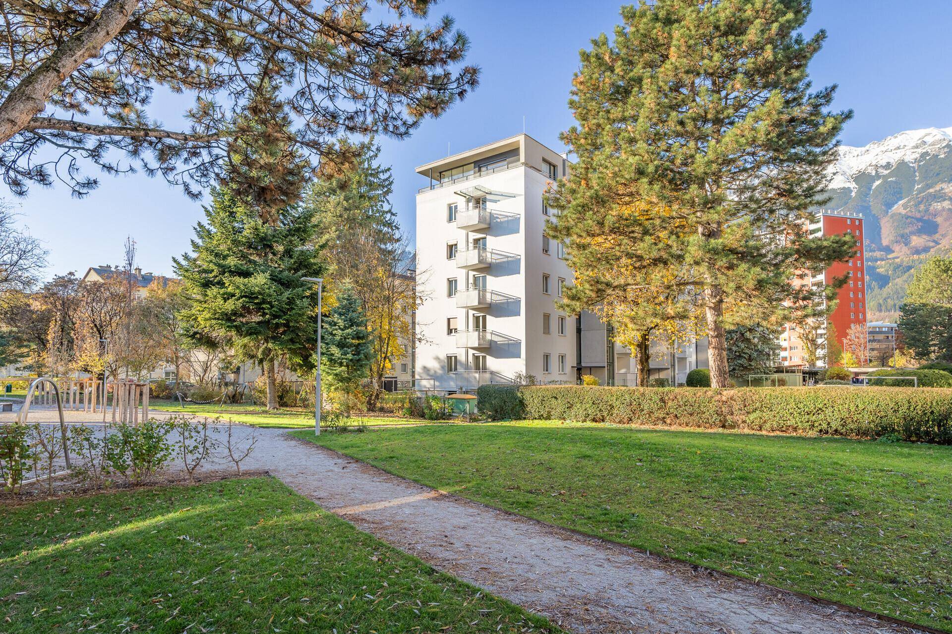 Modernes Wohngebäude mit Balkonen, umgeben von Grünflächen und Bäumen in sonniger Lage.