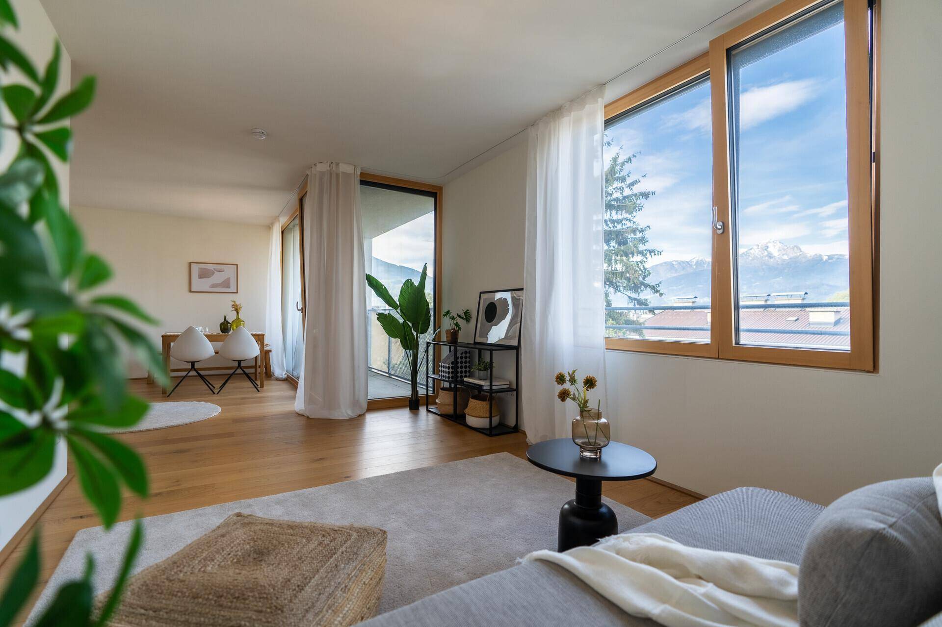 Gemütliches Wohnzimmer mit Sofa, Pflanzen und großen Fenstern mit Bergblick.