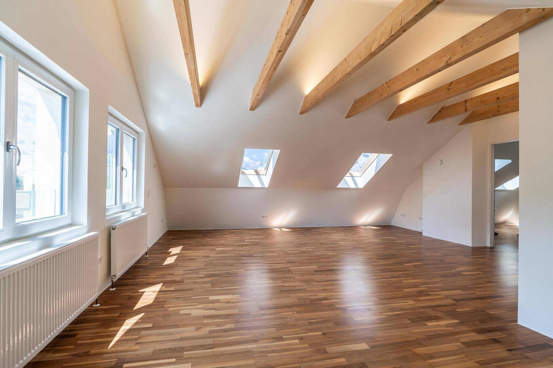Großzügiger Dachbodenraum mit Holzbalken, Parkettboden, großen Fenstern und zusätzlichen Dachfenstern.