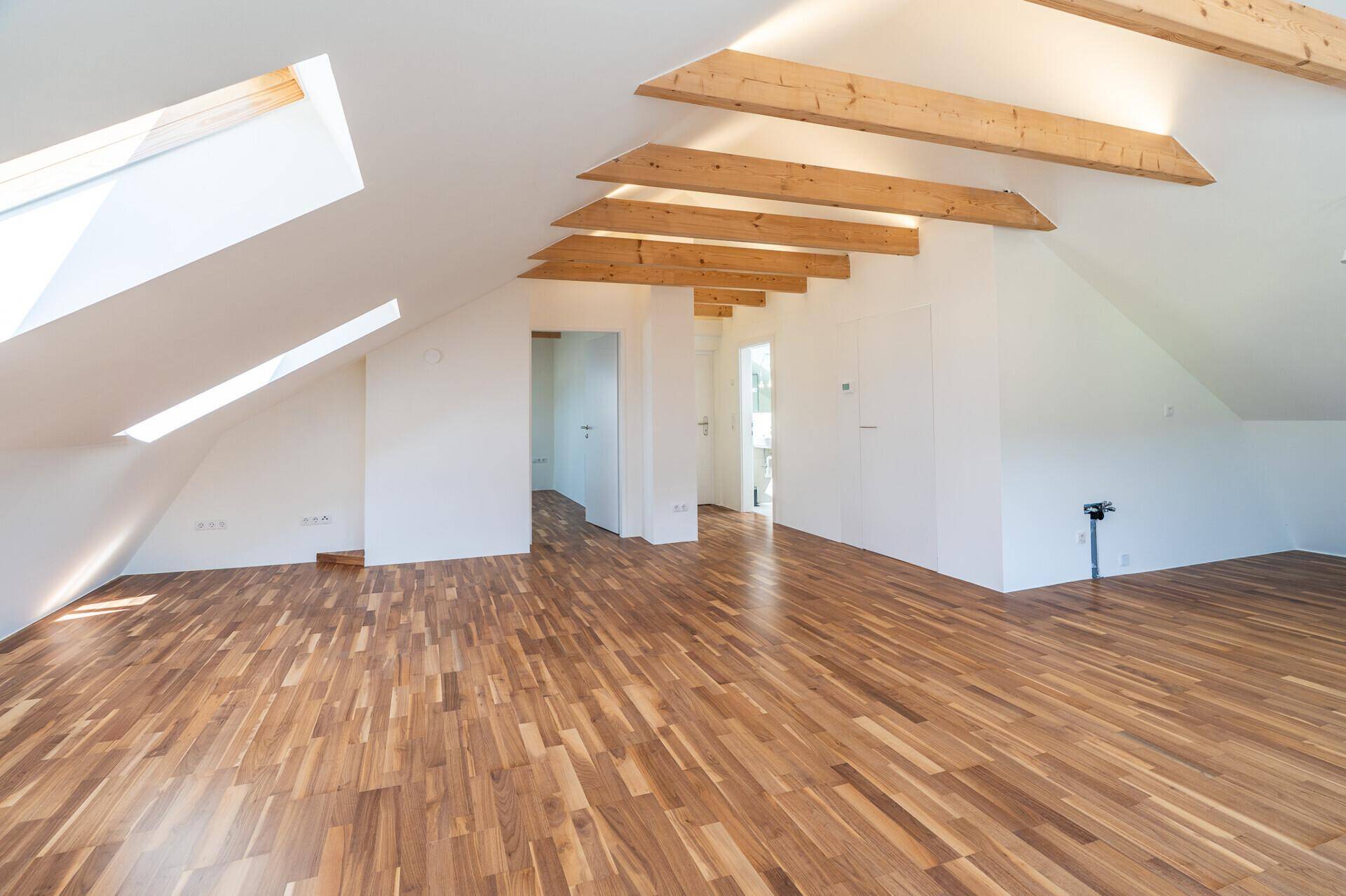 Geräumiges Dachgeschoss mit sichtbaren Holzbalken, Parkettboden und Dachfenstern für viel Licht.