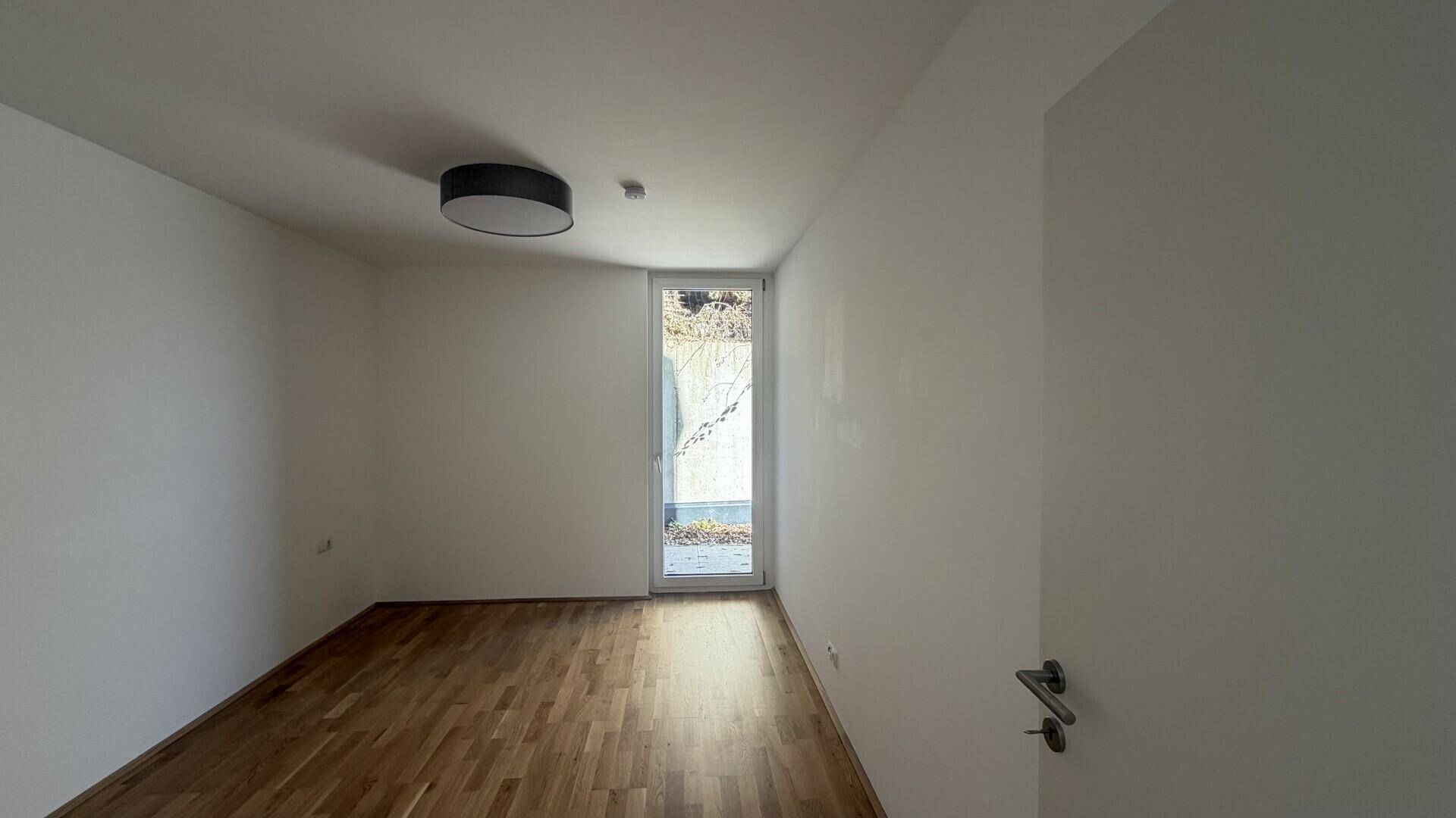 Helles Zimmer mit Holzboden und direktem Zugang zu einem kleinen Außenbereich.