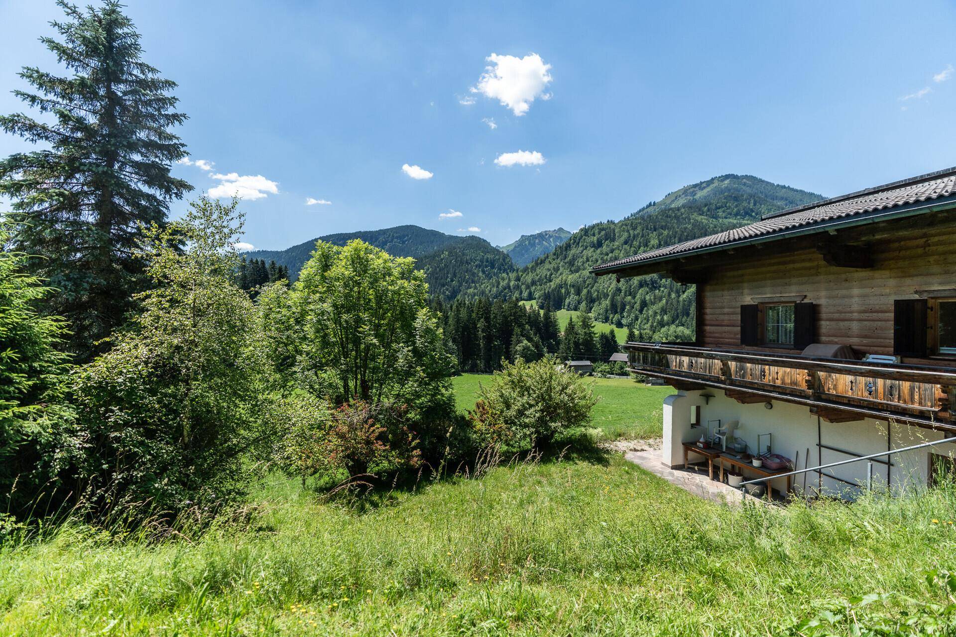 Seitenansicht des Hauses mit Balkon und Blick auf die umliegende grüne Natur und Berge.